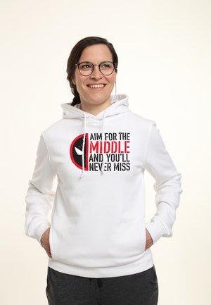 Smilende person med briller iført en hvid hættetrøje med teksten "Sigt mod midten, og du vil aldrig misse" og en rød og sort grafik.