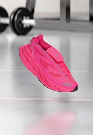 Chaussure de sport rose vif avec un design élégant et courbé, des panneaux en maille et une semelle en caoutchouc. Comprend une bride à velcro et des éléments réfléchissants.