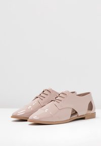 Chaussures Oxford en cuir verni rose pâle, à bout pointu, avec un design à lacets et des panneaux latéraux découpés, dotées d'une semelle plate.