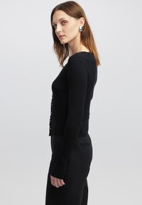 Schwarzer, gerippter Cardigan mit langen Ärmeln, rundem Ausschnitt und Knopfverschluss vorne. Der Stoff ist weich und hat eine taillierte Passform.