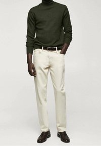 Dunkelgrüner Strickrollkragenpullover, cremefarbene Hose, brauner Gürtel und braune Loafers. Glatte Textur, figurbetonte Silhouette und neutrale Farbgestaltung.