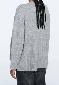 Gray knitted sweater with a loose fit, ribbed texture, wide sleeves, and a high-low hem detail. Back view shows a minimalist design.