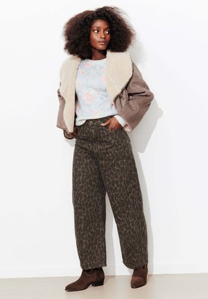 Veste marron surdimensionnée avec un col en shearling crème, pull léger à motifs floraux, et pantalon ample vert foncé à imprimé léopard. Bottines marron.