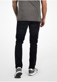 Čierne rifľové nohavice so slim fit strihom, s dvoma zadnými vreckami a šikmým šitím. Nosí sa s šedými a bielymi športovými topánkami.