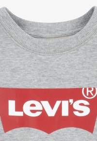 Šedá mikina s žebrovaným kulatým výstřihem. Na prsou se nachází velké červené logo "Levi's" v bílé barvě na měkké bavlněné směsi.