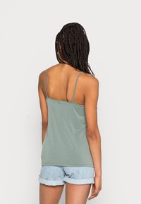 Ljusgrön ärmlös topp med tunna remmar, tillverkad av mjukt material, i kombination med uppvikta denimshorts. Enkelt design, utan mönster.