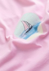 Burāks ar sarkani balti svītrainu buru peldošs uz zila ūdens, attēlots uz krokaina gaiši rozā auduma fona.