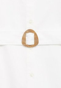 Weißes Hemd mit einer großen, ovalen, hellbraunen Schnalle an der Taille und einer glatten Stoffstruktur mit kleinen Knöpfen.