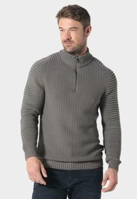 Grau gestrickter Pullover mit hohem Kragen und halbem Rei�ßverschluss, der strukturierte Rippenverzierungen an den Schultern und Ärmeln sowie einen taillierten Saum aufweist.