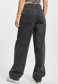 Wide-leg jeans made of dark gray denim, featuring back pockets, a high waist, and a clean finish. Textured fabric with a relaxed fit.