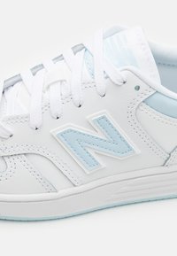 Valged tossud heledate siniste aktsentidega, tekstuuriga nahast, lamedate paeltega ja silmapaistva embosseeritud "N" logoga. Kujundatud kontrastõmblustega.