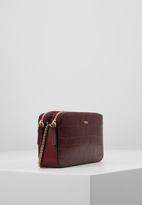 Burgundin nahkainen olkalaukku, jossa on krokotiilikuosiset pinnat, kultaiset yksityiskohdat ja kaksoisterilukkosijat. Varustettu irrotettavalla ketjuhihnalla.