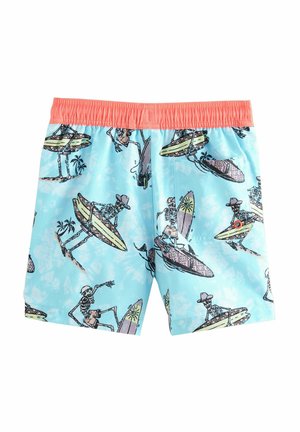 Blaue Badeshorts mit einem korallenfarbenen elastischen Bund, der ein Muster von Skeletten zeigt, die auf verschiedenen Surfboards gegen einen hellen, bewölkten Hintergrund surfen.