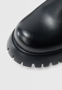 Cizme negre din piele cu vârf rotund, finisaj texturat și talpă groasă din cauciuc cu margini zimțate pentru o prindere îmbunătățită.