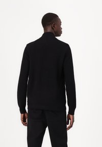 Black knit sweater with a high collar, ribbed texture, and long sleeves, displayed from the back against a white background.