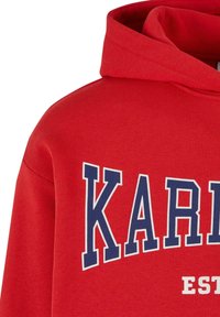Červená mikina s kapucňou vyrobená z jemného materiálu s veľkými modrými nápismi "KARL" a detailmi "EST", s uvoľneným strihom a klasickým tvarom.