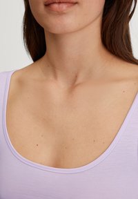 Lilac scoop-neck top made of smooth fabric, featuring a fitted design and minimal stitching details, highlighting a clean neckline.