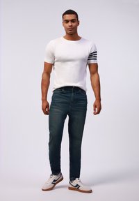 Camiseta de punto blanca de manga corta con rayas negras, jeans azul oscuro y zapatillas blancas con acentos azules y suela marrón.