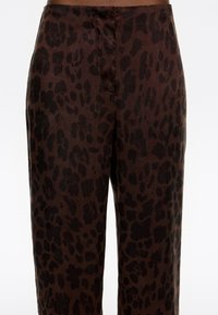Hnedé nohavice s potlačou leopardieho vzoru v čiernej farbe. Tkanina má hladký povrch, uvoľnený strih a prirodzený spád.