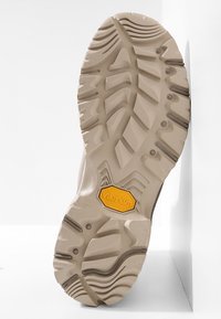 Podešev Vibram, béžová barva, s vícesměrnými vzory běhounu a žlutým hexagonálním logem. Hladký povrch s texturovanými úchopy.