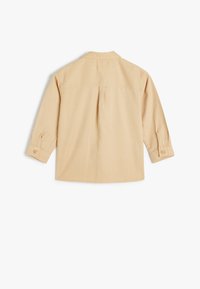 Camicia beige a maniche lunghe con colletto, polsini abbottonati e dettagli di cucitura sulla spalla. Realizzata in un tessuto morbido e testurizzato. Vista posteriore mostrata.