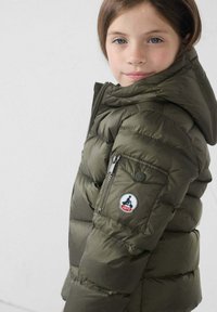 Olijfgroene gewatteerde jas met een capuchon, voorzien van ritszakken en een logo patch op de mouw. Gladde textuur en doorgestikte design.