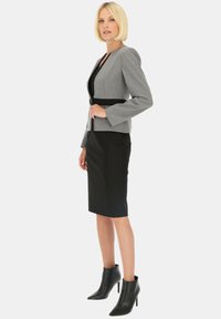 Szary dopasowany żakiet z czarnym paskiem, zestawiony z czarną spódnicą ołówkową i czarnymi botkami na obcasie, zaprezentowany na modelce.