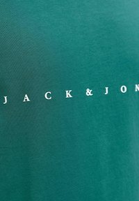 Groen katoenen T-shirt met een gladde textuur en een bedrukt ontwerp van de merknaam "JACK & JONES" in het wit, horizontaal uitgelijnd.