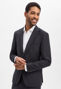 Dark gray tailored blazer with notch lapels, single-button closure, and subtle texture. Worn over a white collared shirt.