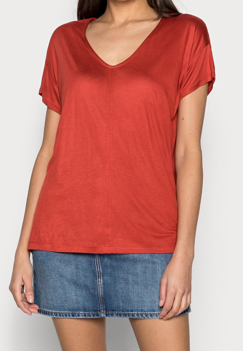 T-shirt rouge léger à manches courtes et col en V, fabriqué en tissu lisse, associé à une mini-jupe en denim avec une couture centrale et un ourlet cousu.