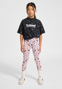 Czarny krótki t-shirt z powtarzającym się wzorem logo. Jasnoróżowe legginsy z pasującymi nadrukami logo. Białe trampki i teksturowane skarpetki.