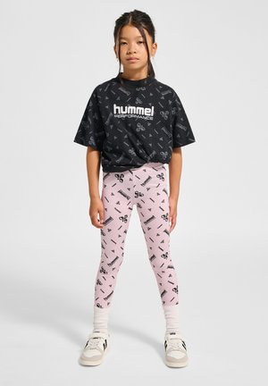 Svart t-shirt med kort ärm och upprepat logomönster. Ljusrosa leggings med matchande logotryck. Vita sneakers och texturerade strumpor.