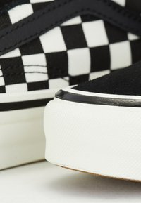 Gros plan de baskets à carreaux noirs et blancs montrant une semelle extérieure en caoutchouc blanc texturé et une tige en daim noir cousue.