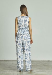 Blumenoverall in Weiß mit blauen Mustern, mit einem taillierten Oberteil, Peplum-Taille und weitem Bein. Glattes Material mit weichem Finish.