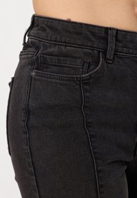Jeans de ganga preta com uma cintura alta, corte reto e bolsos minimalistas, com um acabamento texturizado e costura combinada.