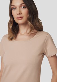 Beżowa koszulka z krótkim rękawem i okrągłym dekoltem. Materiał wydaje się miękki i gładki, z dopasowanym krojem. Brak widocznych wzorów lub akcentów.