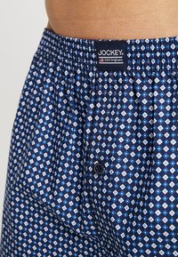 Kampanjbyxor i marinblått mönster med en diamantdesign i vitt och ljusblått. Elastisk midja med en Jockey-logotyp och en knäppning.