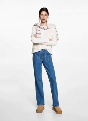Weißes Langarmoberteil mit rundem Ausschnitt, leicht gestreifter Schal über den Schultern drapiert, blaue weitgeschnittene Jeans und beige Plateauschuhe.