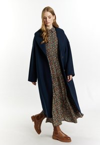 Námornícky vlněný kabát s oversized klopami, květinové maxi šaty s detailem na zkracování a hnědé kotníkové boty s masivní podešví.