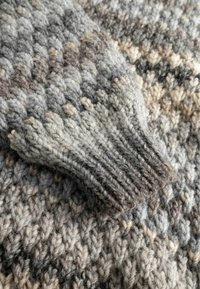 Maglione lavorato a maglia con polsino a coste, caratterizzato da un motivo strutturato nelle tonalità di grigio, beige e marrone, realizzato con filato spesso.