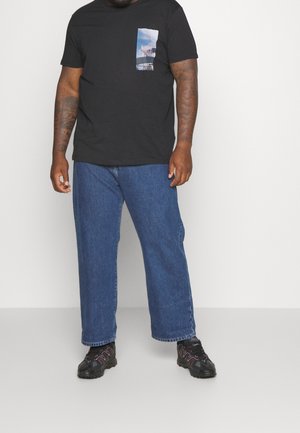 Černé tričko s kulatým výstřihem a kapsou s fototiskem; spárováno s modrými širokými džínami a černými teniskami s červenými akcenty.