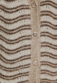 Tissu tricoté beige avec des rayures zigzag marron et trois boutons ronds brillants texturés alignés verticalement sur le devant d'un cardigan.