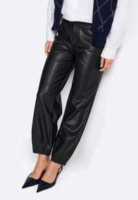 Melnas ādas bikses ar brīvu piegriezumu un sašaurinātiem piedurknēm. Valkātas ar baltu krekls un melniem patentādām augstpapēžu kurpēm.