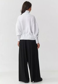 Biały sweter z dzianiny z wysokim kołnierzem i prążkowanym dołem, w połączeniu z luźnymi czarnymi spodniami o szerokich nogawkach. Minimalistyczny design, miękka tekstura.