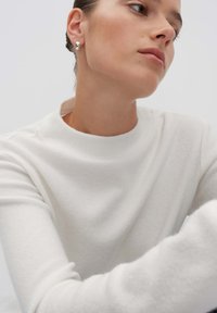 Weißes, geripptes Langarmoberteil mit hohem Kragen. Verfügt über eine glatte Textur und einen lässigen Schnitt, betont durch ein klares Design und subtile Details.
