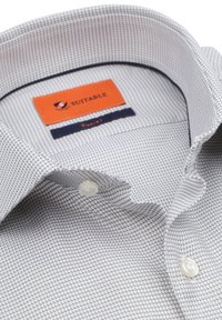 Overhemd met een wit en grijs geometrisch patroon, met een prominente oranje "SUITABLE" label en twee witte knopen.