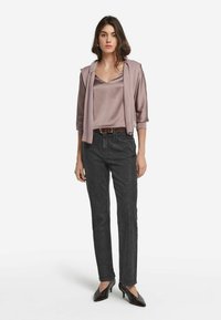 Hellblaue satinierte Bluse mit drei Viertelärmeln, darüber ein passender Pullover, der lässig über den Schultern hängt. Schwarze Jeans im Straight-Leg-Schnitt und spitze Pumps.