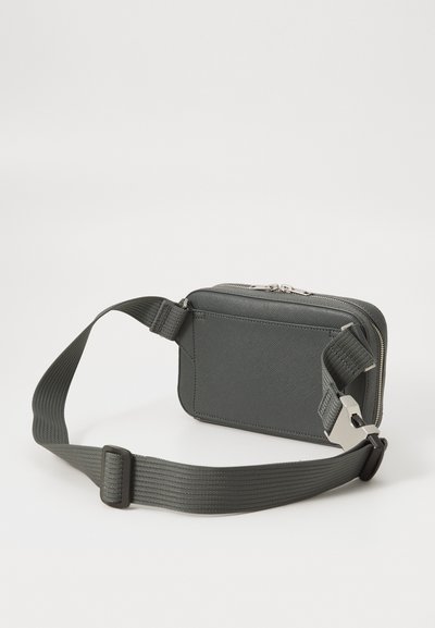 Borsa a cintura rettangolare grigia scura con superficie texture, tracolla regolabile intrecciata, zip argentata e fibbia metallica su uno sfondo neutro.