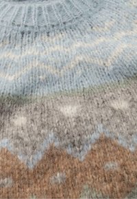 Neulepaita, jossa on pehmeitä, vaaleansinisiä, harmaita ja ruskeita värejä sekä kuvioitu design. Tekstuuri näyttää muhkealta ja lämpimältä.