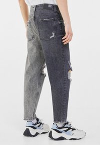 Distressed denim jeans with a two-tone gray design, featuring rips and frayed hems, paired with chunky sneakers.